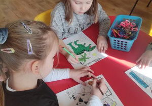Dziewczynki kolorują ilustrację z dinozaurem następnie wykonują puzzle składają je.